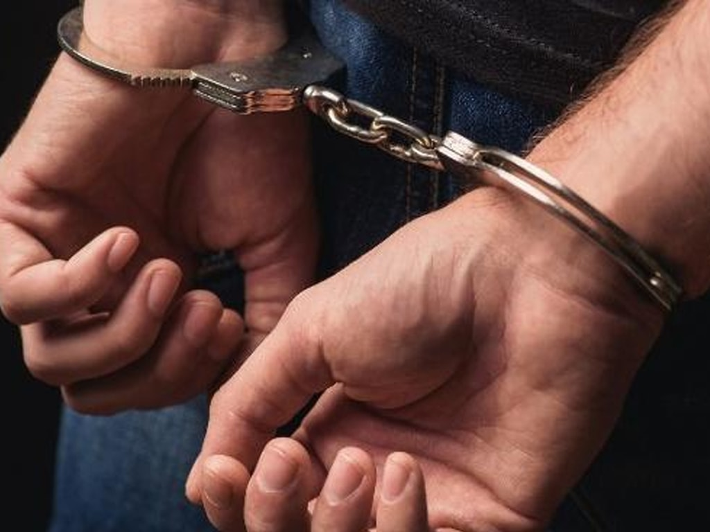 Image shows a figure in handcuffs