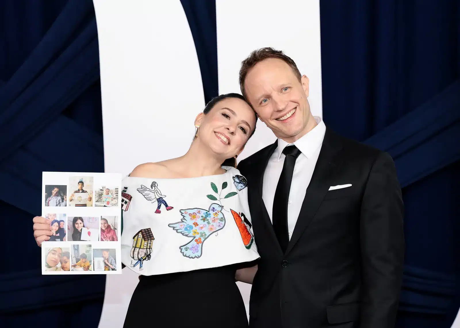 The image shows Miss Rachel holding the drawings made by the children in Gaza.