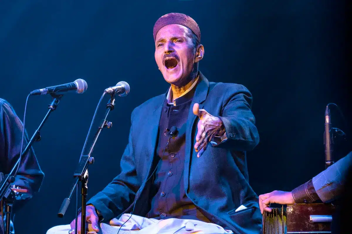 The image shows Ustad Naseeruddin Saami on stage, singing.
